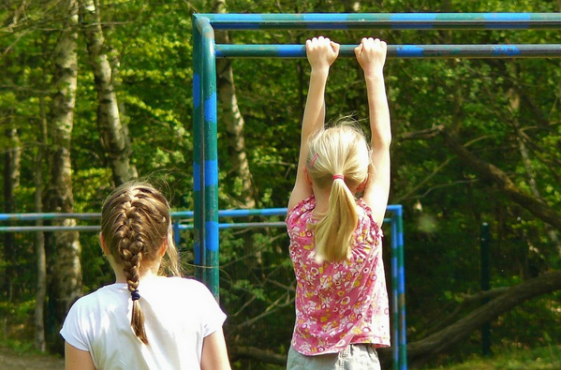 Two girls at the playground playing on the "monkey" bars 