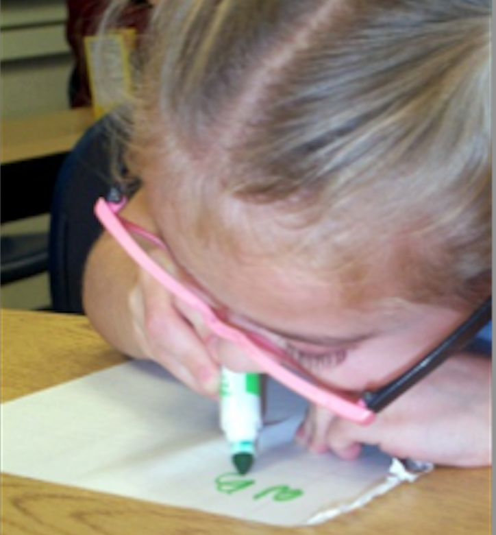 A second grade girl uses a green marker to write