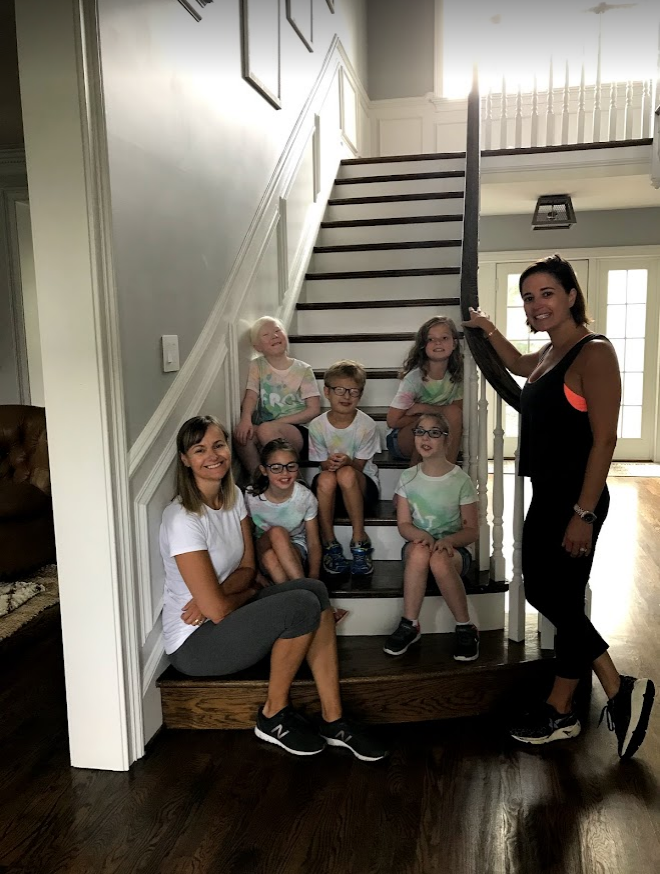 Elementary students sitting on steps at a summer camp wearing the t-shirts they made along with two teachers