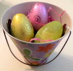 a metal pail decorated with flowers and butterflies filled with yellow and pink plastic Easter eggs