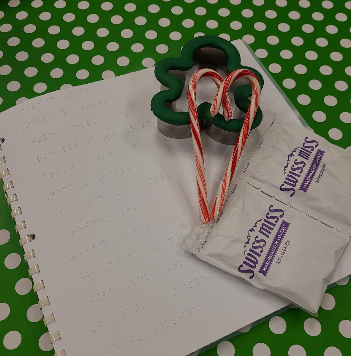 Braille book for holiday songs, hot chocolate packages, cookie cutter, and candy canes 