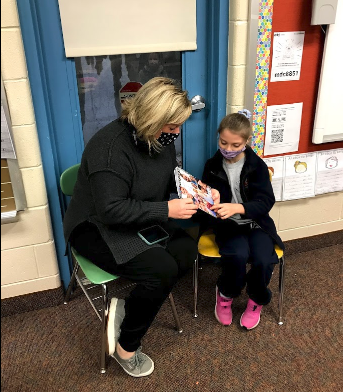 Second grade teacher with her student showing the class her writing folder