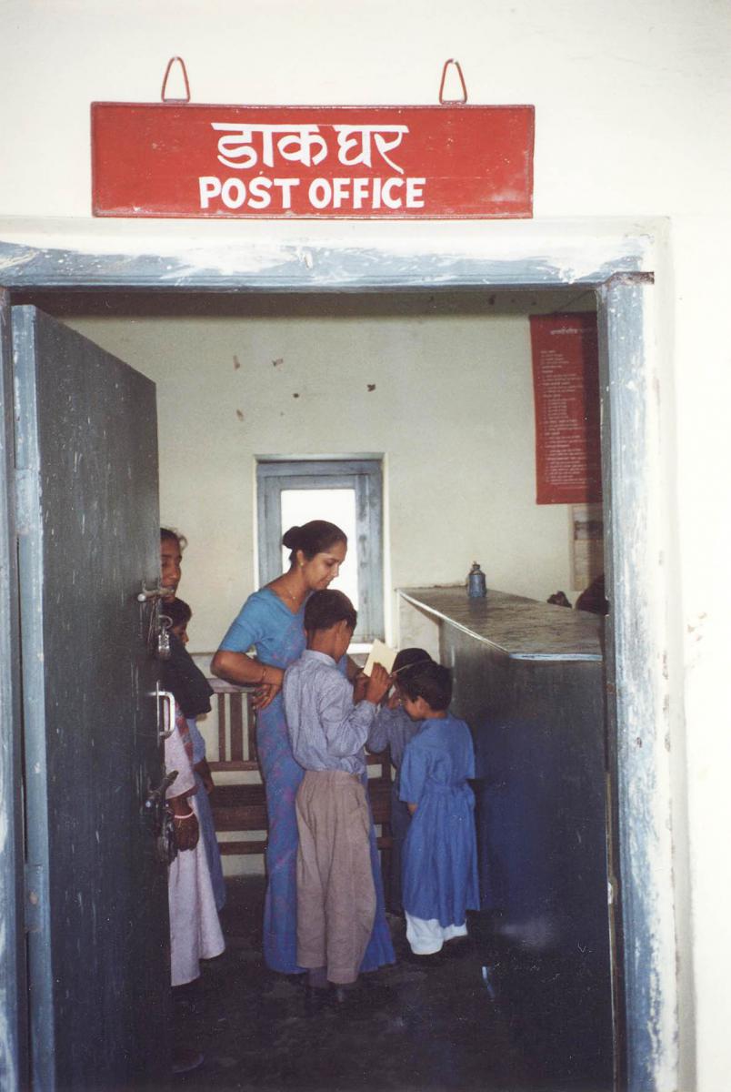 Children in the post office examine with their teacher the postcards that they purchased.