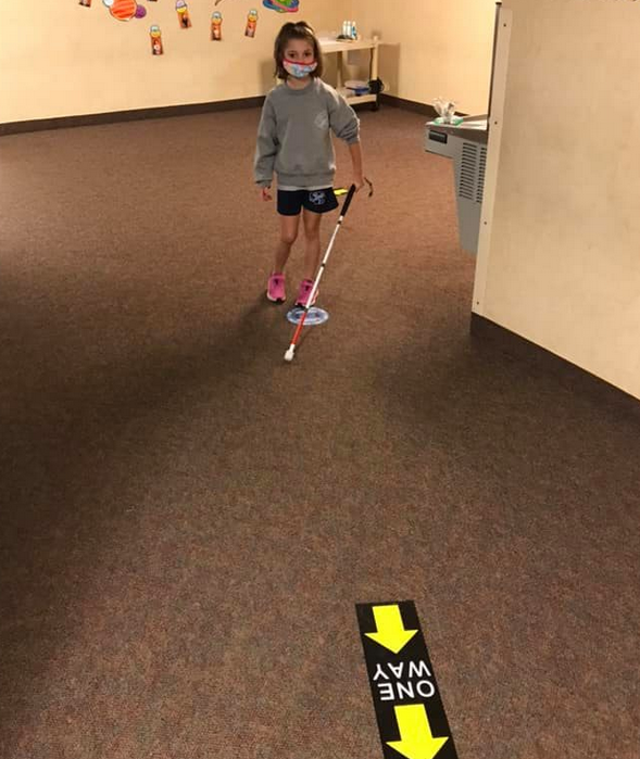 student walking arouond a corner in a school hallway with her cane
