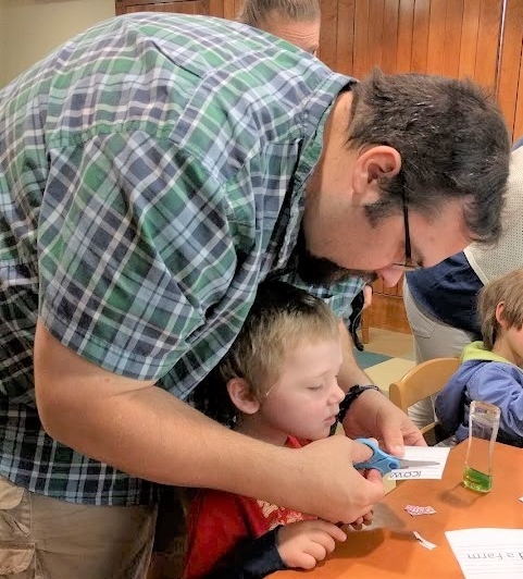 Father leaning over his preschool son during a group craft activity