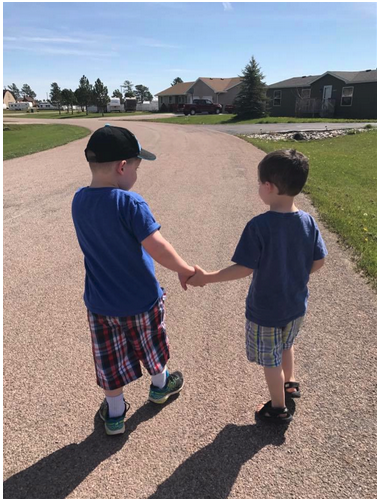 Two young brothers walking down the street in a neighborhood, holding hands on a sunny day. 