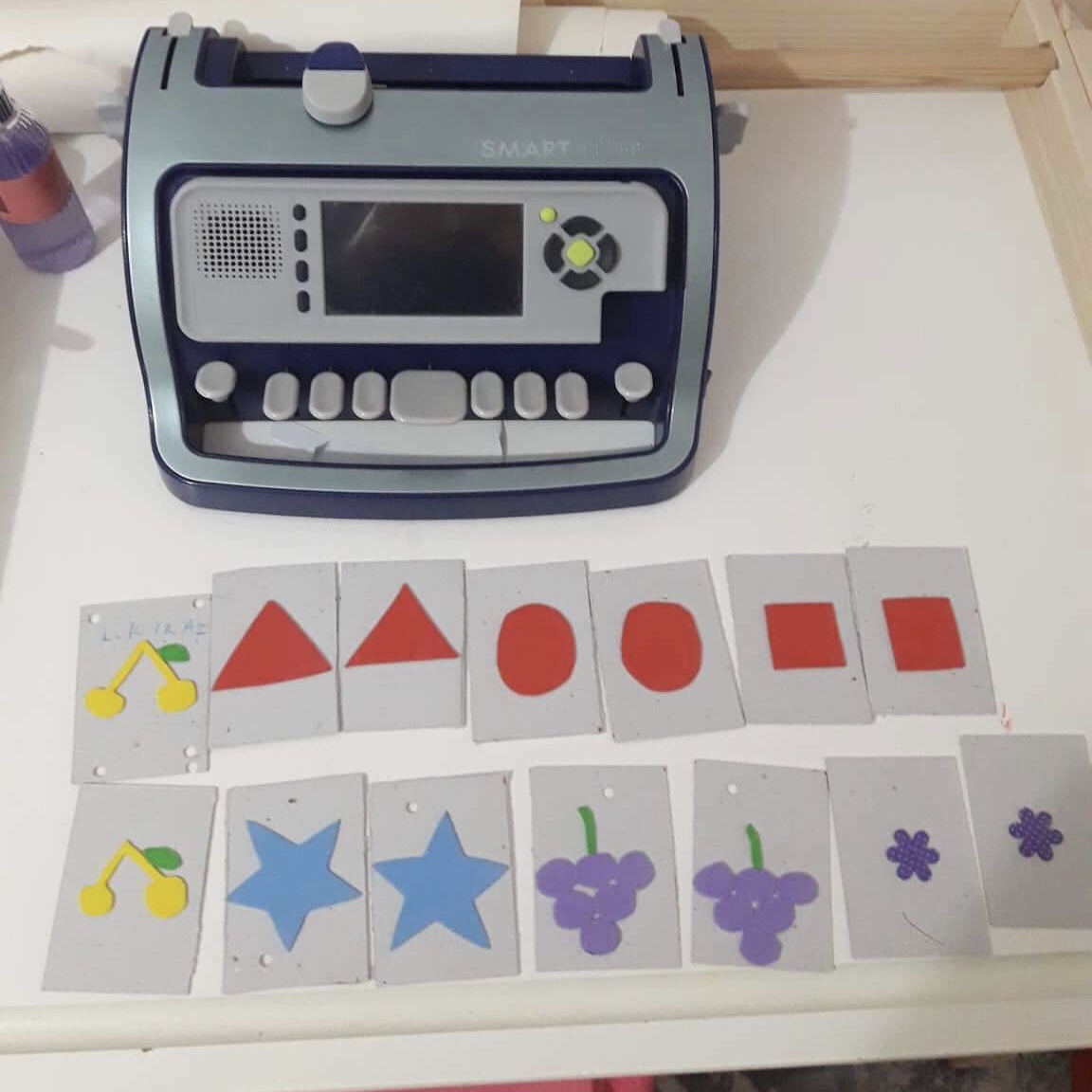 A Smart Brailler in the background with shape matching cards in the foreground