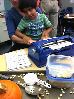 Child sitting with teach receiving "hand-under-hand" access to his braillewriter