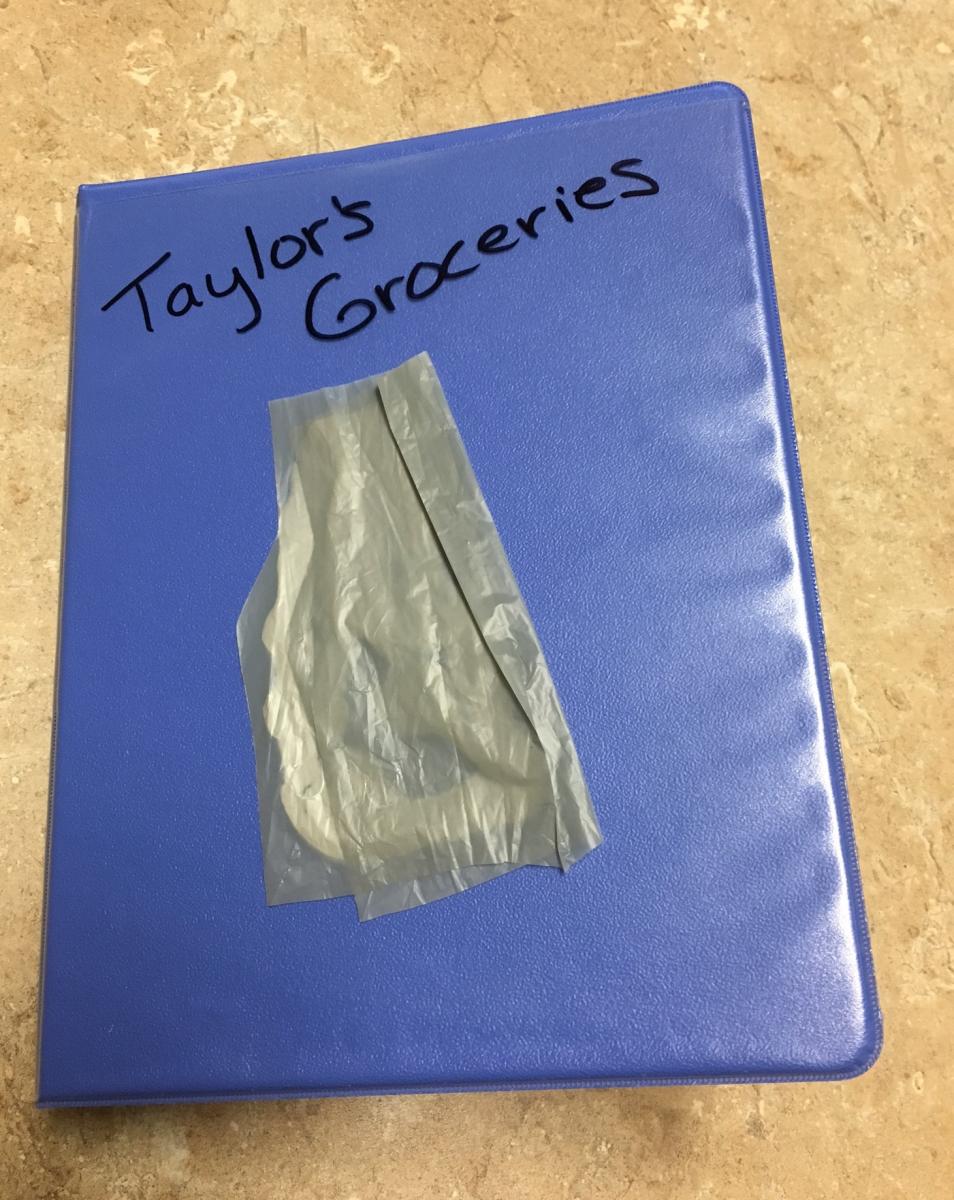 a small binder labeled "Taylor's Groceries" with a piece of a shopping bag on it