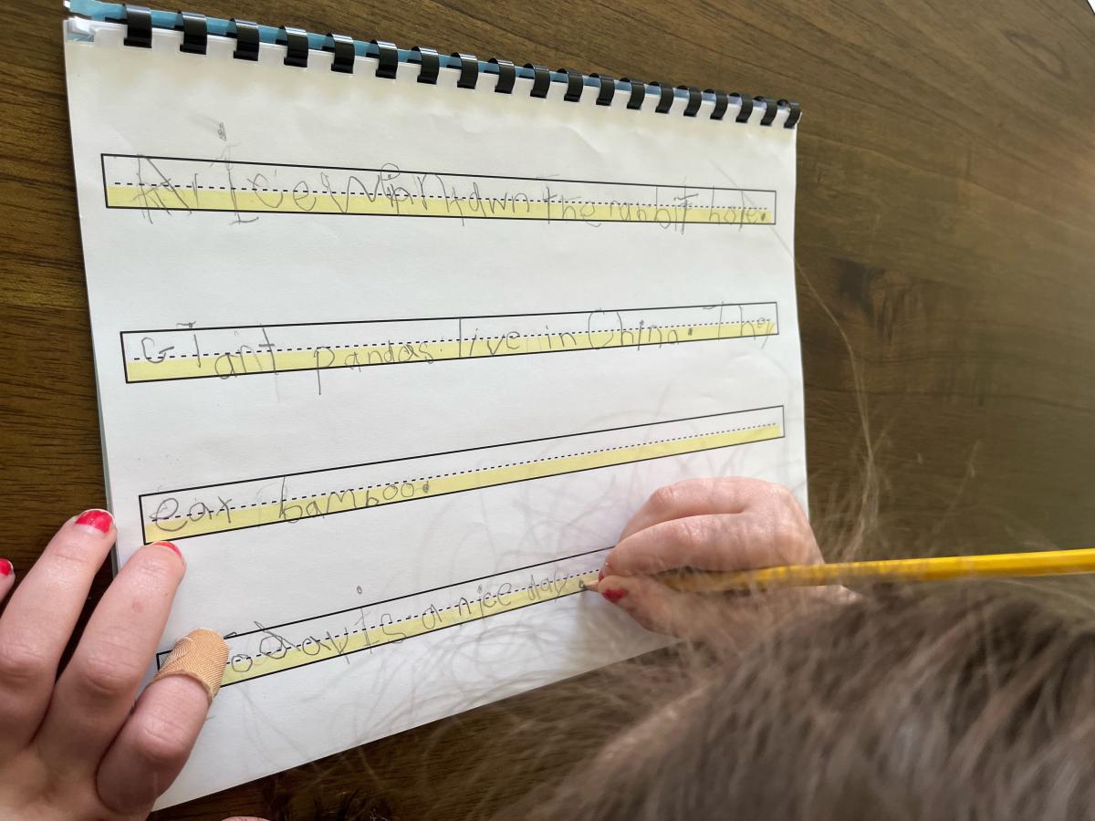 Student writing on a four lined, highlighted piece of paper