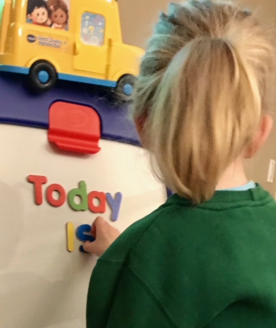 A girl with a pony tail manipulates letters spelling out "Today is"