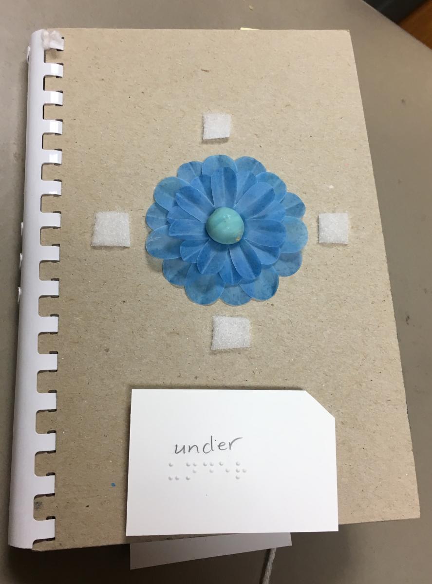 Tactile flower with "under" written in print and braille