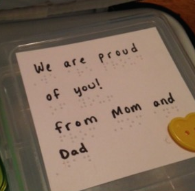 lunch box with braille and text "we are proud of you! from mom and dad"