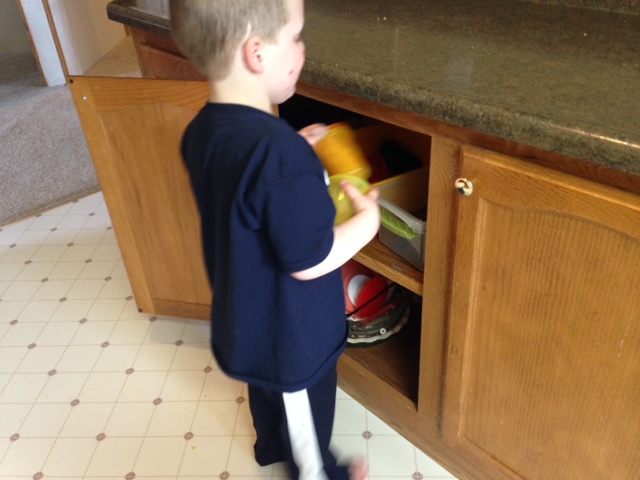 A young boy puts plastic cups away in a cabinet
