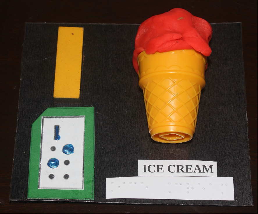 Letter "I" written in print with corresponding braille card and a plastic ice cream cone