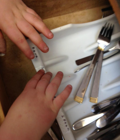 Utensil sorter with braille labels and a child's hand sorting