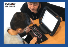 Student typing on an adapted keyboard with teacher assisting