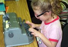 A young girl uses a braillewriter