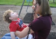 a young woman is sitting on a swing with a child in her lap, facing her