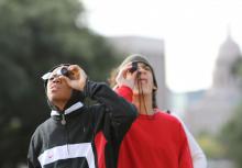 Two boys look through monoculars outdoors.