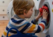 A young boy putting clothes into the washing machine