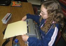A girl putting braille paper into her Perkins braillewriter