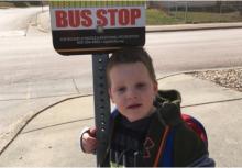 A boy stands at a bus stop.