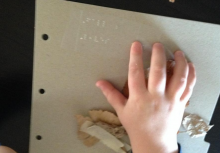 A child's hand reads braille about fall leaves