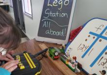 A young girl with glasses using APH Braille Buzz and lego station