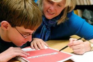 A boy with glasses looks at a line of print with his teacher.