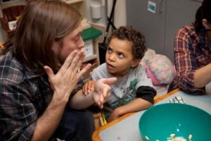 A young boy watches attentively as adult signs to him.