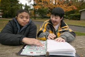 Two boys look at a book of picture symbols together.