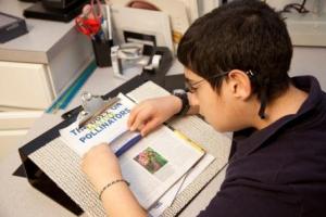 Boy uses handheld magnifier to read a line of print.