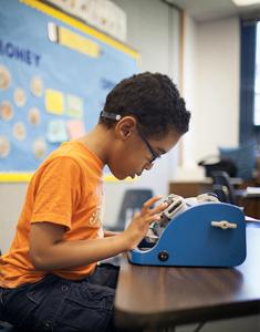 A boy with glasses writes on a Smart Brailler