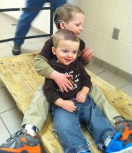 Two young boys sit on a wooden cart