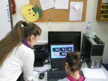 A girl sits in front of a computer screen as an adult leans over next to her.