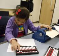 A girl uses an abacus and a braille writer.
