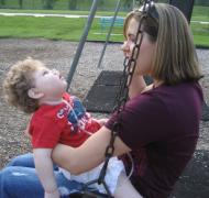 a young woman is sitting on a swing with a child in her lap, facing her