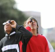 Two boys look through monoculars outdoors.