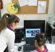 A girl sits in front of a computer screen as an adult leans over next to her.