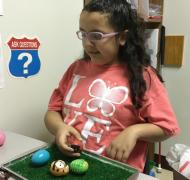 A girl places Easter eggs on a grass tray.