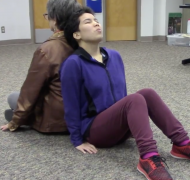 two people sitting on the floor leaning back-to-back