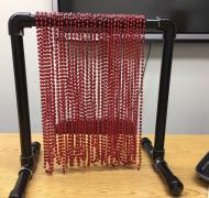 A PVC easel painted black with red bead necklaces hanging down from it.