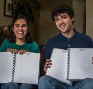 A student holds up her braille year book next to her twin brother
