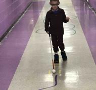 A young boy walks in a school corridor using his cane