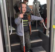A young boy steps down out of a bus while holding his cane