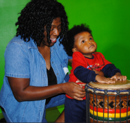 A young child plays the drum with his mother