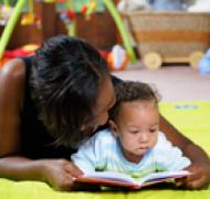 Woman reads with a baby while lying on the floor.