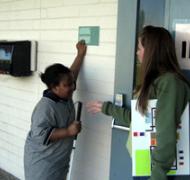 Image of 4th grade student feeling a braille sign while instructor looks on.