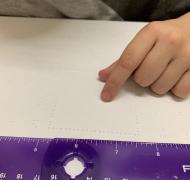 Hand on paper with braille with purple ruler at top of paper